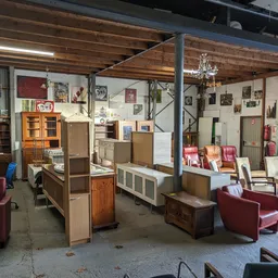 Ruime winkelvloer met diverse meubels, fauteuils en kasten uitgestald, houten plafond met industriële balken