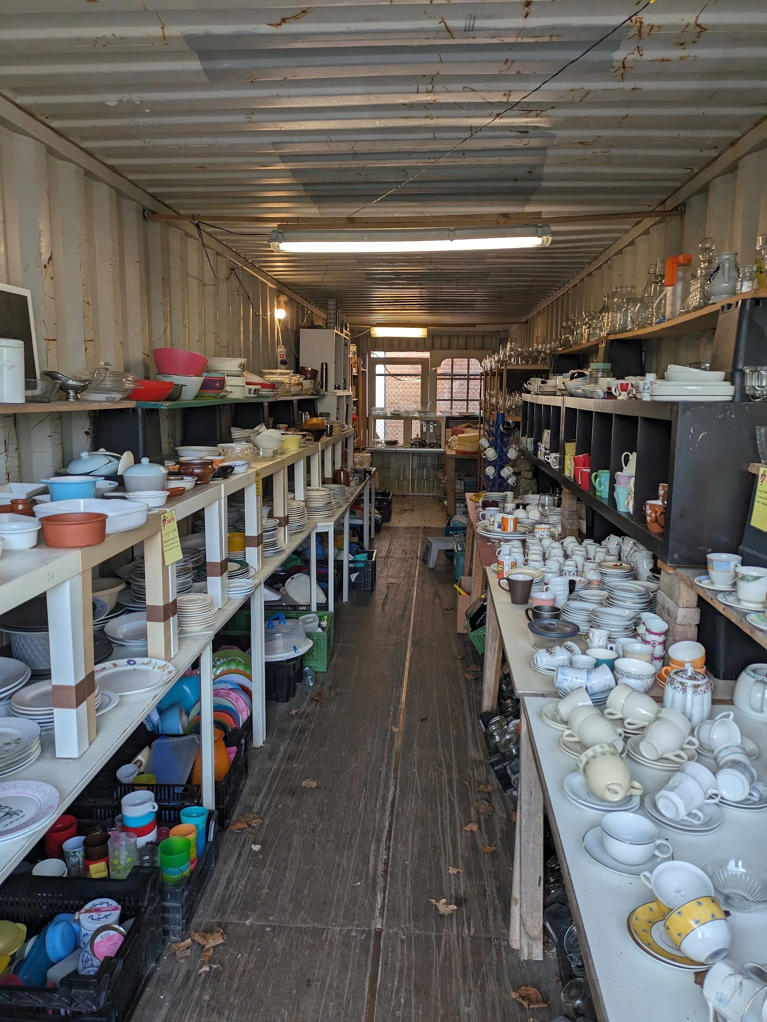 Lange gang in kringloopwinkel met stellingen vol servies, borden, kopjes en huishoudelijke artikelen