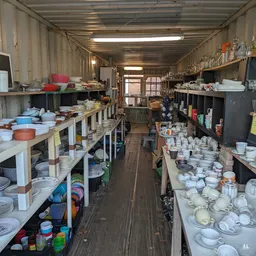 Lange gang in kringloopwinkel met stellingen vol servies, borden, kopjes en huishoudelijke artikelen