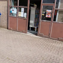 Voorkant van een kringloopwinkel met rode deuren, etalageramen en informatieborden