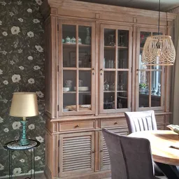 Woonkamerinrichting met houten vitrinekast, behang met bloemenpatroon, vintage lamp en rieten hanglamp