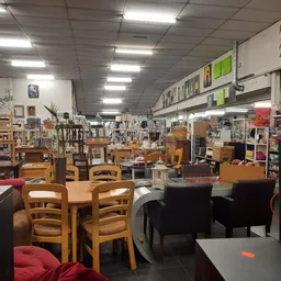 Winkelvloer met houten stoelen, tafels en diverse meubels en huishoudartikelen uitgestald onder fluorescerend licht