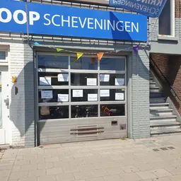 Winkelgevel van Gloop Scheveningen met donkergrijs/zwarte puiframen, witte bakstenen gevel en blauwe winkelnaambord