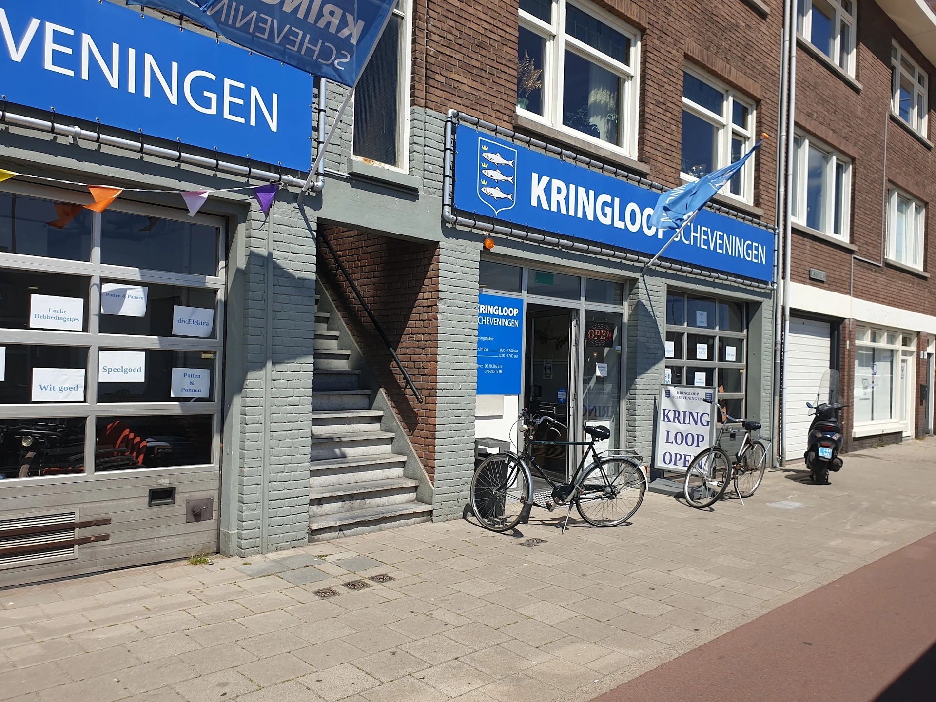 Gevel van Kringloop Scheveningen met blauwe uithangbord, etalageruiten en fietsen ervoor