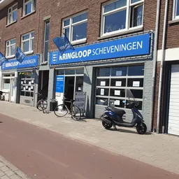 Gevel van kringloopwinkel met blauwe uithangbord 'Kringloop Scheveningen', fiets en scooter ervoor