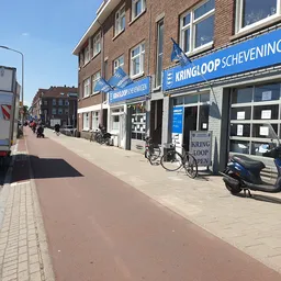 Gevel van Kringloop Scheveningen aan de Westduinweg met blauwe uithangbord, winkelpui en fietsen ervoor
