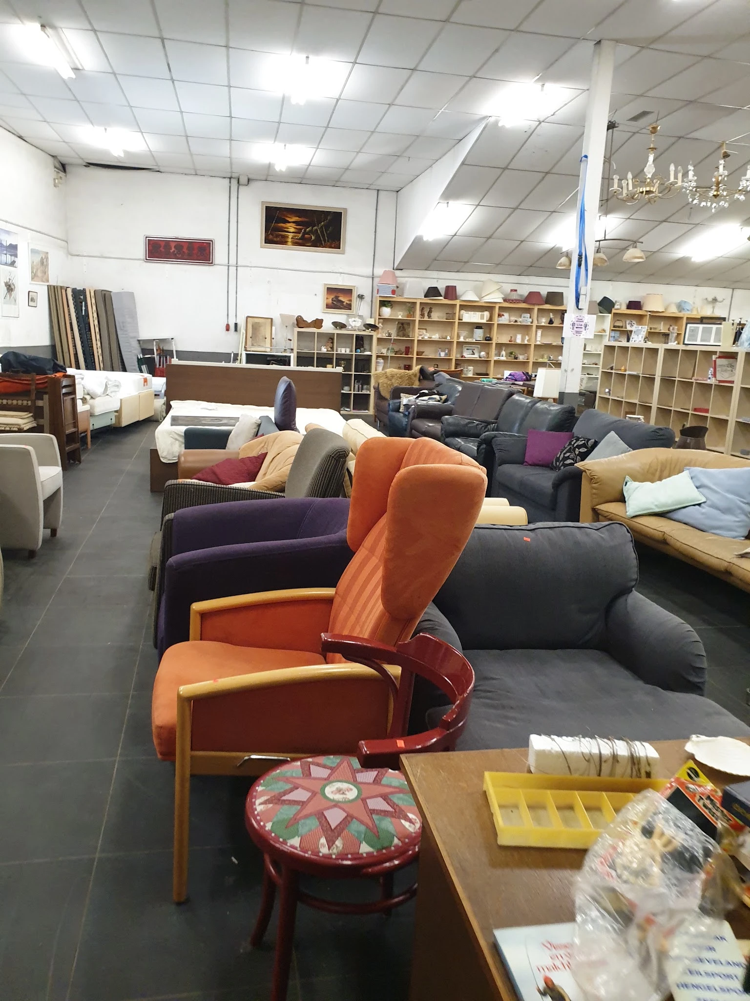 Verschillende tweedehands meubels en fauteuils uitgestald in de winkel, waaronder oranje en paarse stoelen