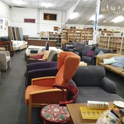 Verschillende tweedehands meubels en fauteuils uitgestald in de winkel, waaronder oranje en paarse stoelen
