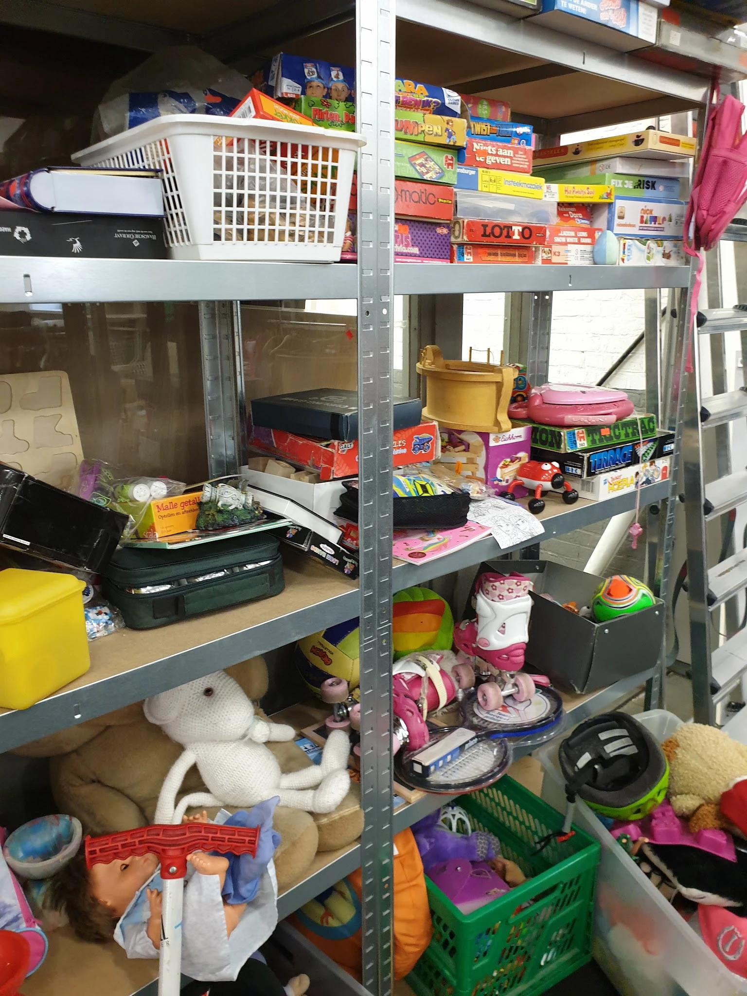 Metalen stellingen volgestapeld met diverse huishoudelijke spullen, dozen en speelgoed in een kringloopwinkel
