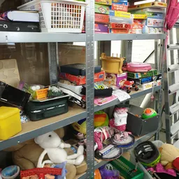 Metalen stellingen volgestapeld met diverse huishoudelijke spullen, dozen en speelgoed in een kringloopwinkel