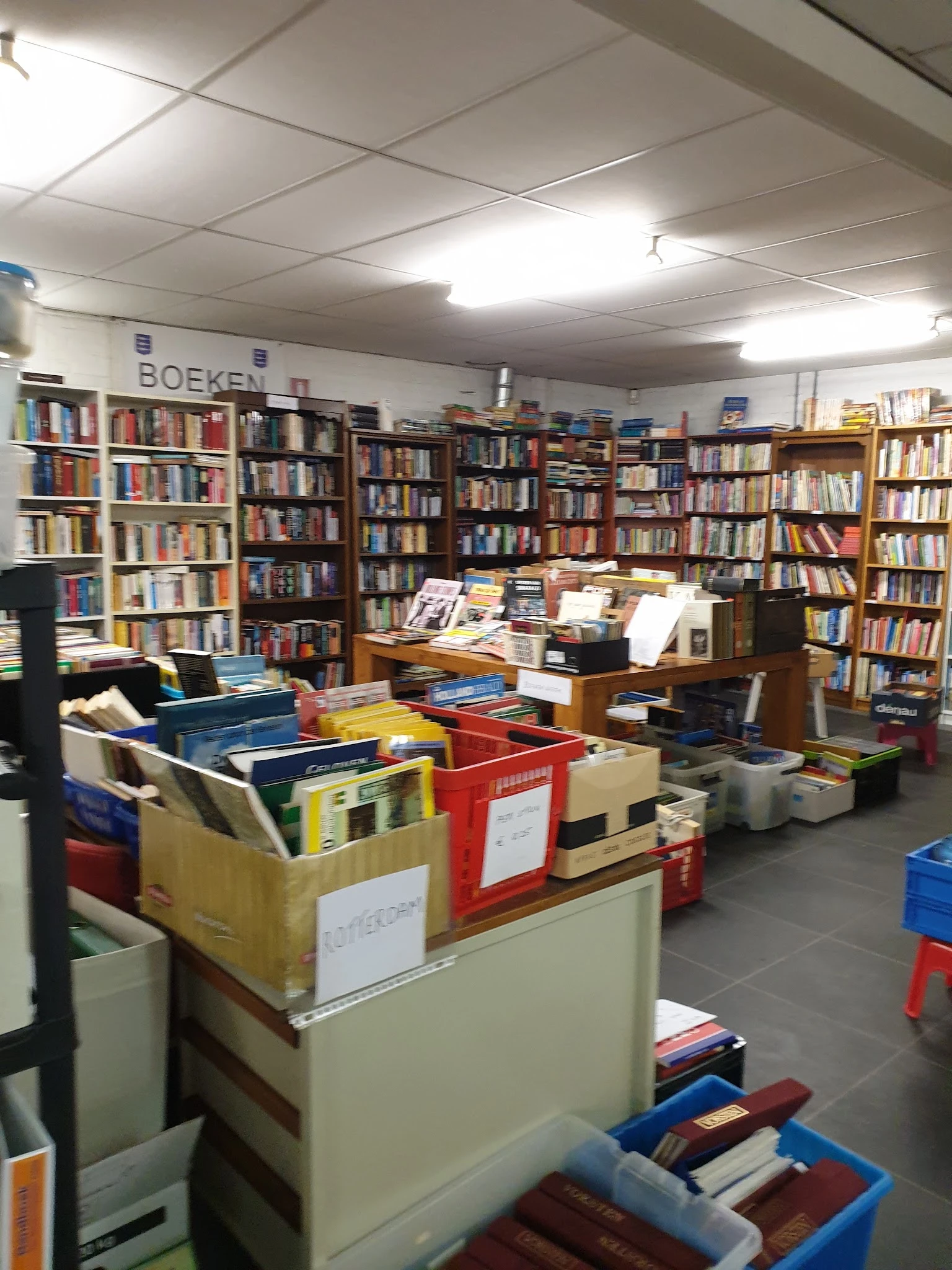Winkelvloer van kringloopwinkel met boekenkast vol boeken en rode en blauwe sorteerkisten op de voorgrond