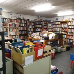 Winkelvloer van kringloopwinkel met boekenkast vol boeken en rode en blauwe sorteerkisten op de voorgrond