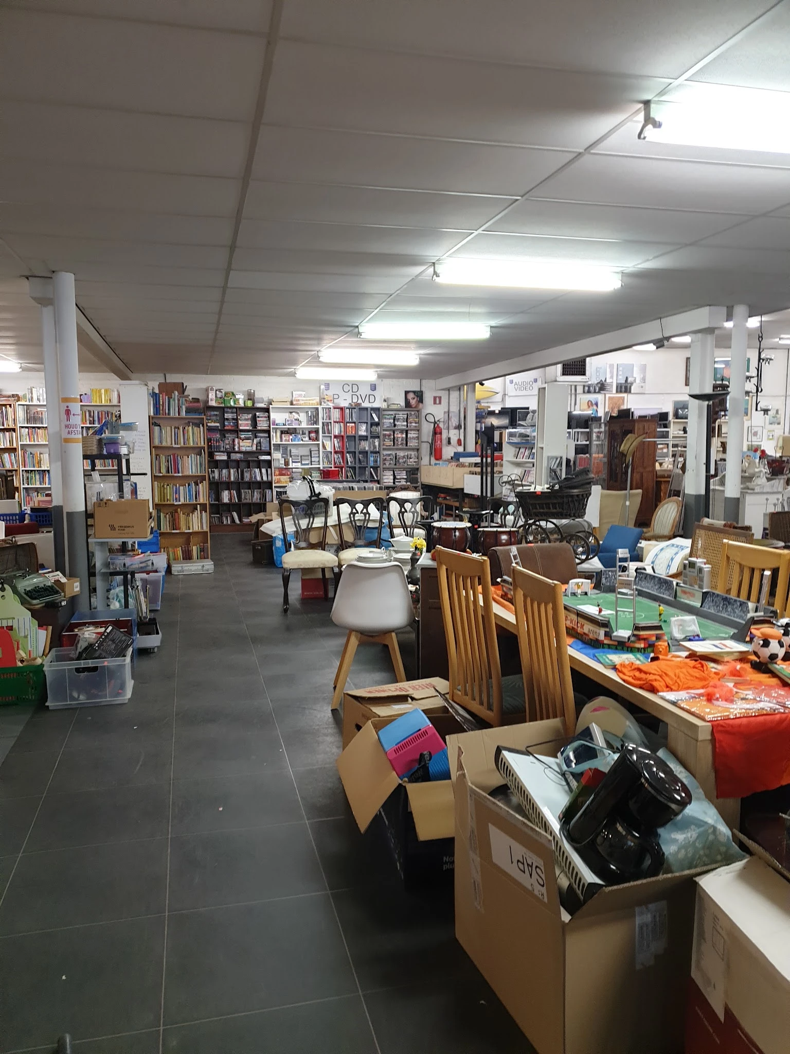 Winkelvloer met boekenkasten, tafels, stoelen en dozen met spullen in een kringloopwinkel