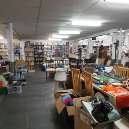 Winkelvloer met boekenkasten, tafels, stoelen en dozen met spullen in een kringloopwinkel