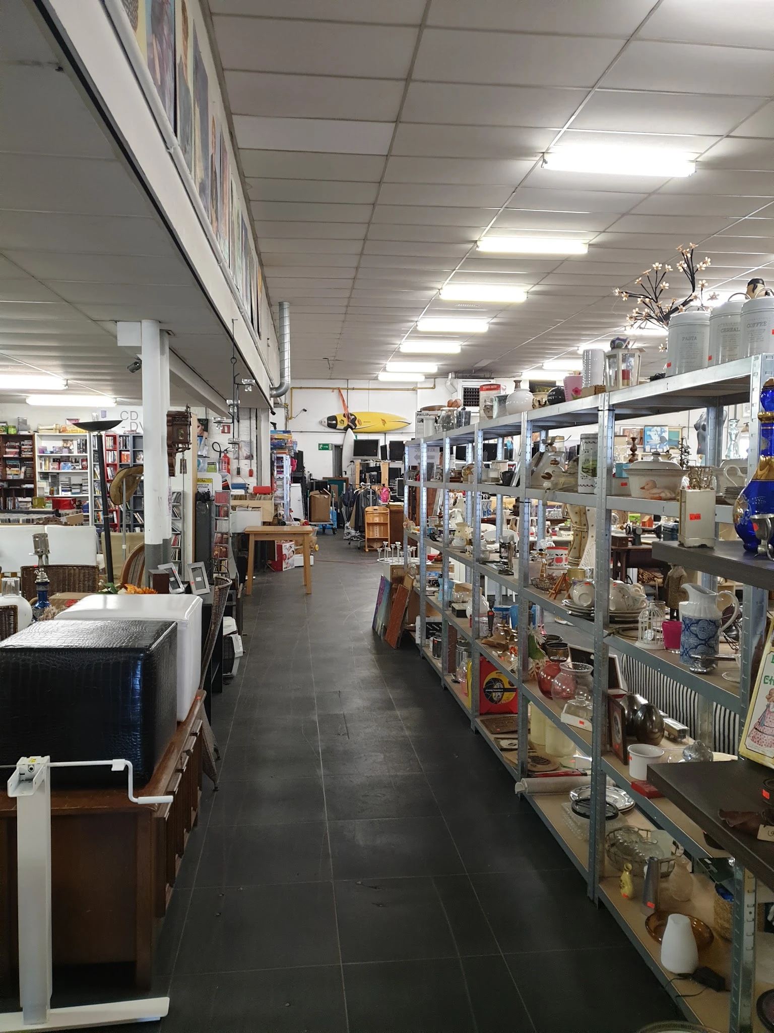 Winkelinterieur met stellingen vol spullen, verlichte plafondpanelen en diverse tweedehands artikelen