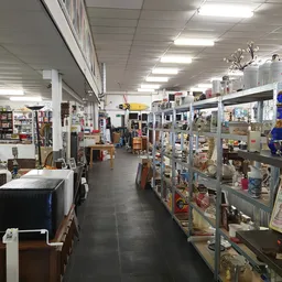 Winkelinterieur met stellingen vol spullen, verlichte plafondpanelen en diverse tweedehands artikelen