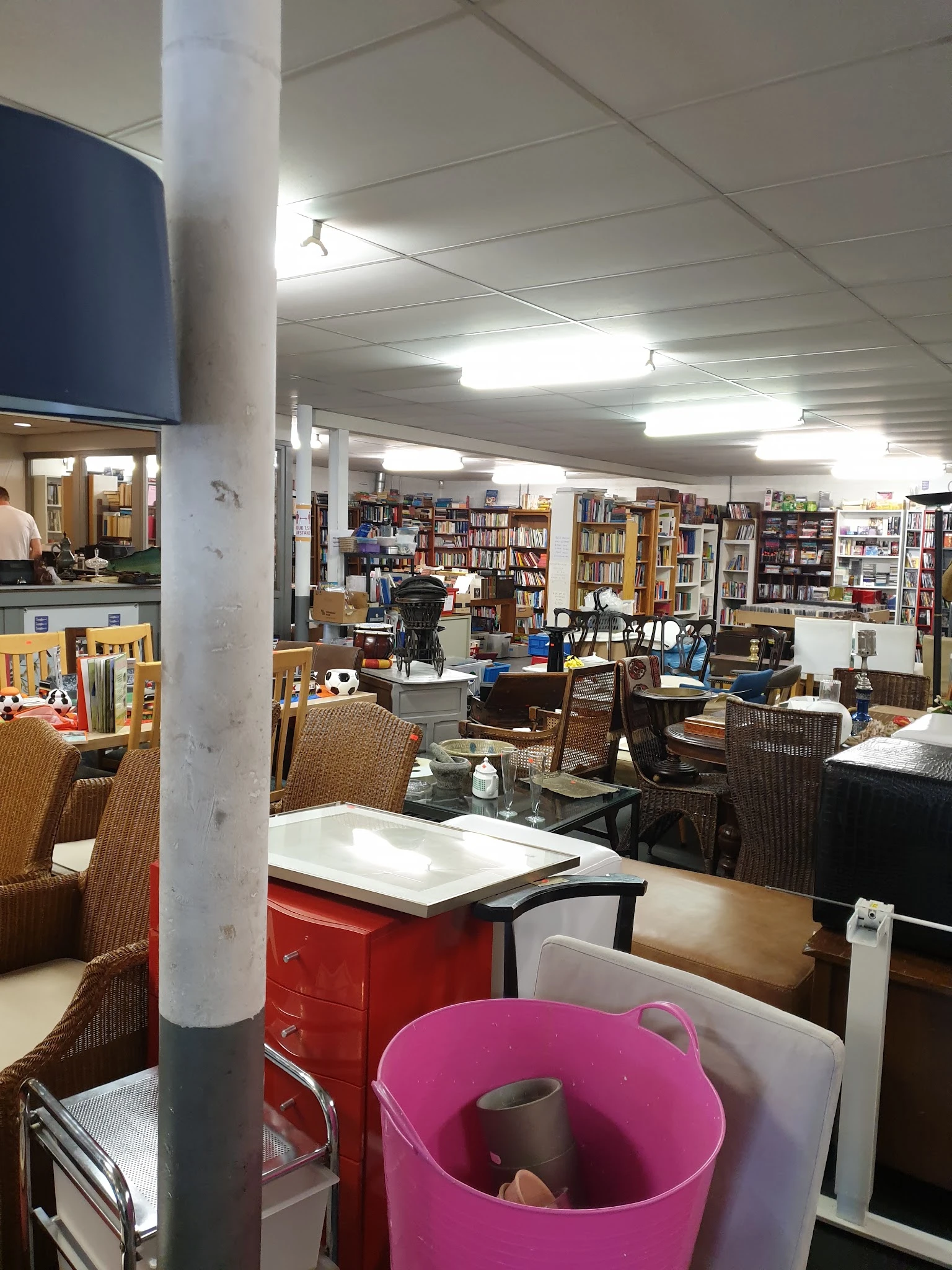 Winkelvloer met boeken in kasten, zithoeken met stoelen en tafels, diverse meubels en spullen