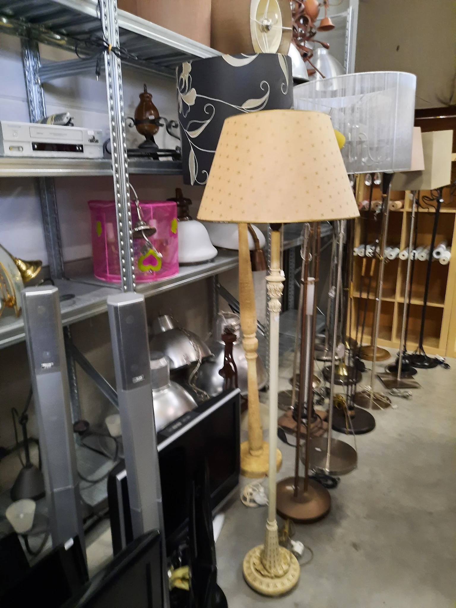 Stellingen met tweedehands huishoudartikelen en een tafellamp met beige kap op voorgrond
