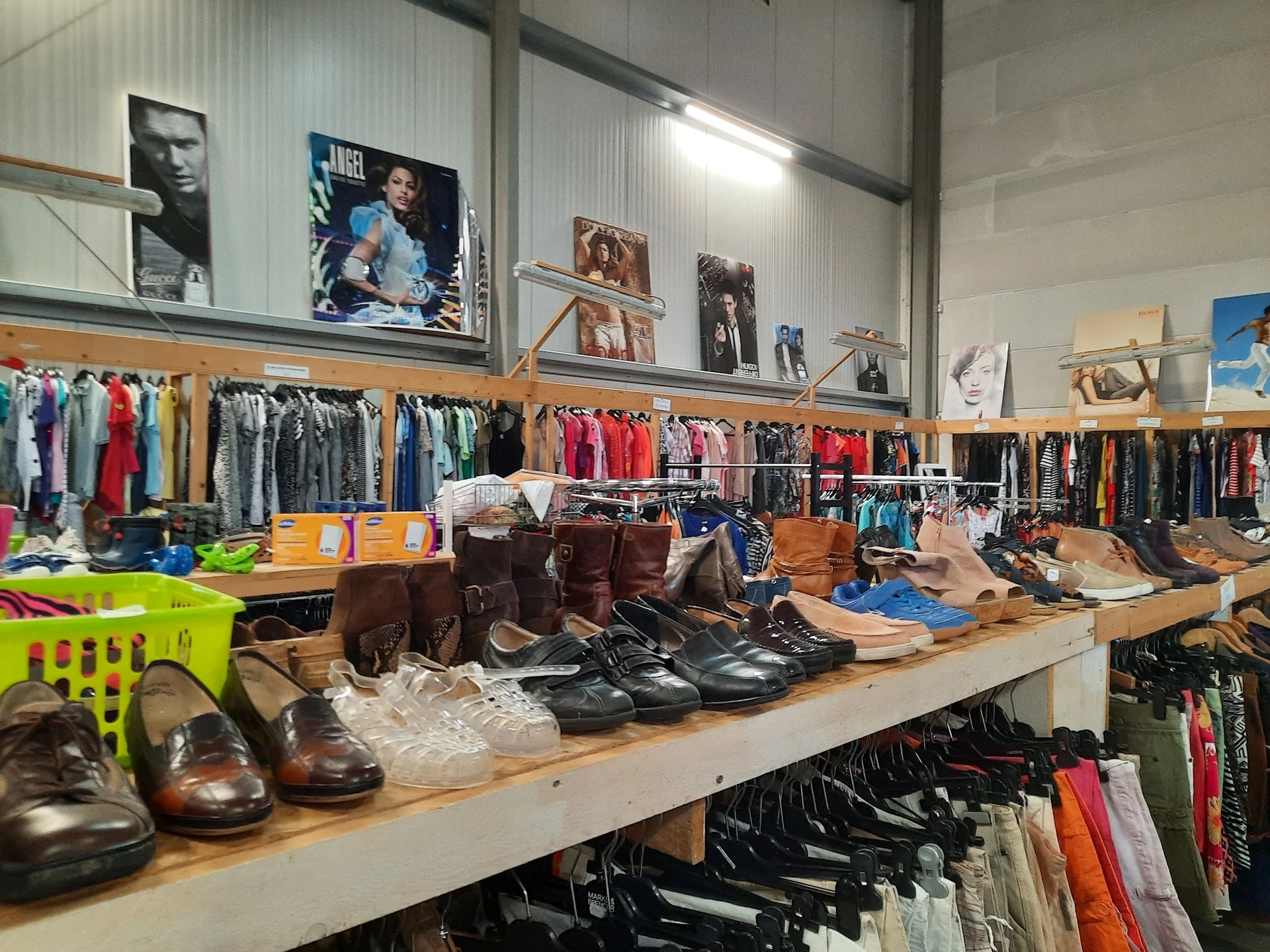 Toonbank met bruine en zwarte schoenen, daarachter rekken met kleding en bovenaan aan de muur foto's en affiches