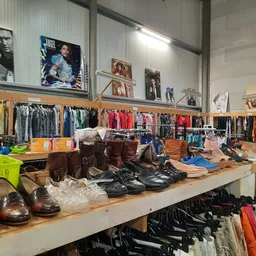 Toonbank met bruine en zwarte schoenen, daarachter rekken met kleding en bovenaan aan de muur foto's en affiches