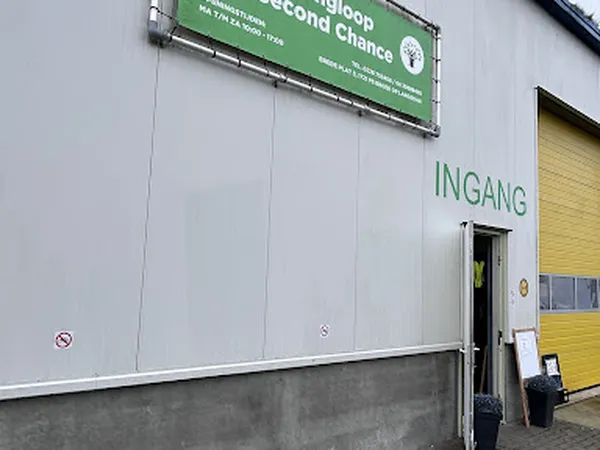 Witte gevel van kringloopwinkel met groen bord en 'INGANG' opschrift