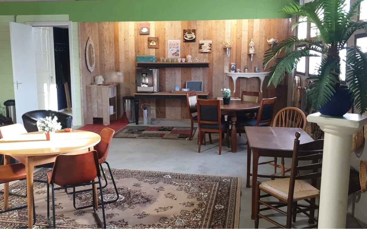 Winkelvloer met houten wanden, verschillende meubelstukken, tafels met stoelen, stellingen met decoratieve items en een groen