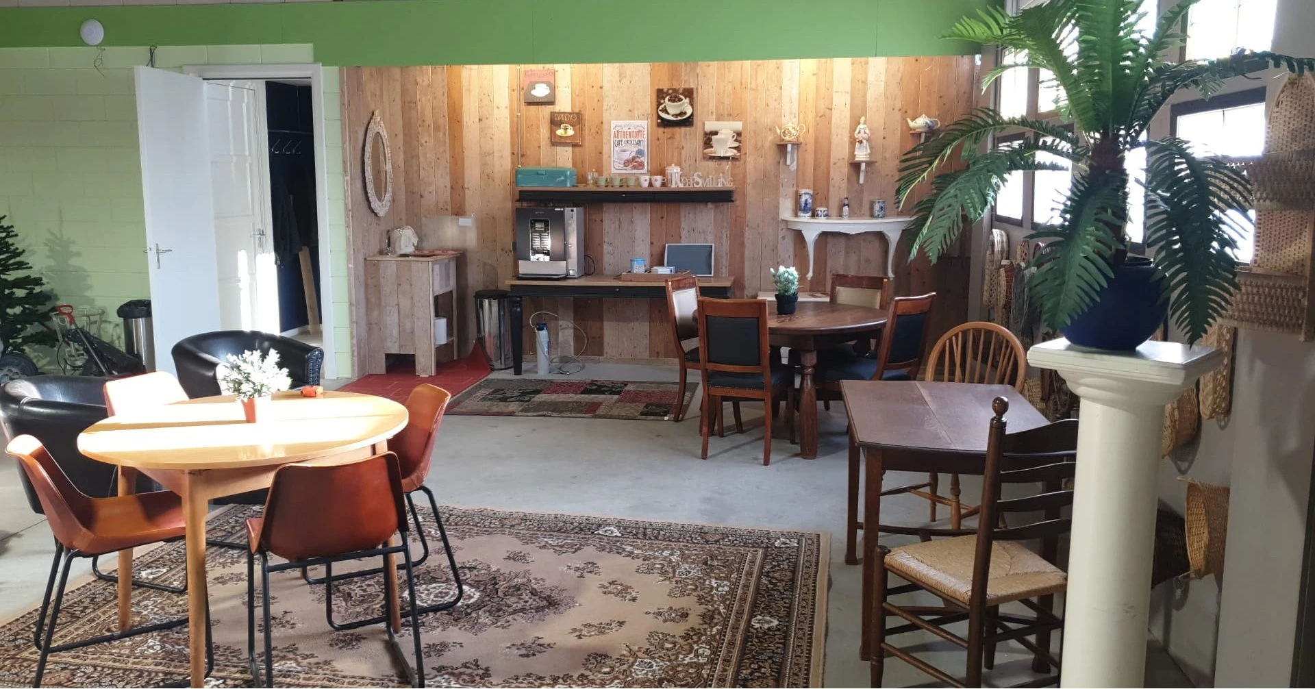 Winkelvloer met houten wanden, verschillende meubelstukken, tafels met stoelen, stellingen met decoratieve items en een groen