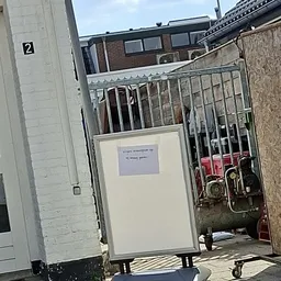 Ingang van kringloopwinkel met een wit bord en gesloten hek, met opgestapelde spullen zichtbaar op de achtergrond