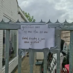 Handgeschreven bericht op papier geplakt op een groene tuinpoort met sluitingstijden