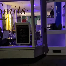 Winkelruit met paarse verlichting en 'Smits' logo zichtbaar, vitrine met spullen en deur