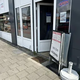 Ingang van kringloopwinkel met witte deuren, opensteld bord en informatieborden aan de gevel