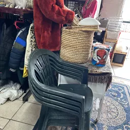 Uitgestalde spullen in kringloopwinkel: zwarte kunststof stoelen, rotan mand, kleding en diverse artikelen
