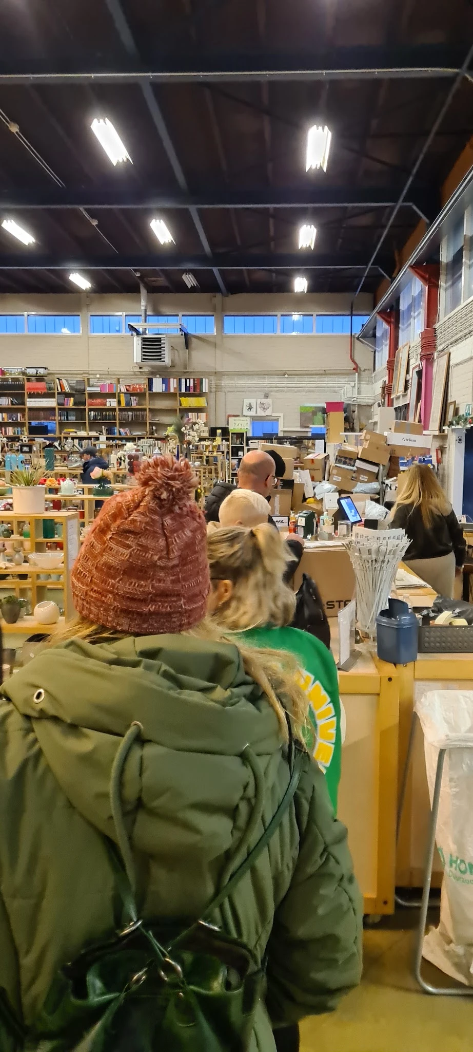 Winkelvloer van kringloopwinkel met bezoekers, boekenkasten, toonbanken en diverse spullen