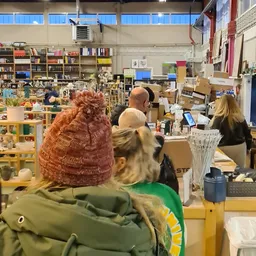 Winkelvloer van kringloopwinkel met bezoekers, boekenkasten, toonbanken en diverse spullen