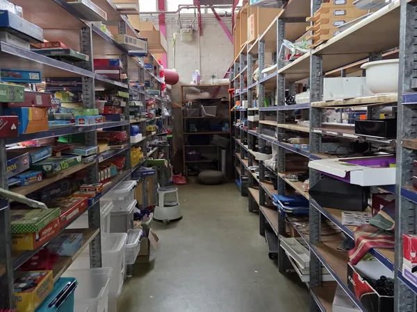 Winkelgang met metalen stellingen aan beide zijden vol met diverse spullen en dozen