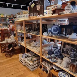 Houten stellingen met serviesgoed, borden en decoratieve items in een kringloopwinkel