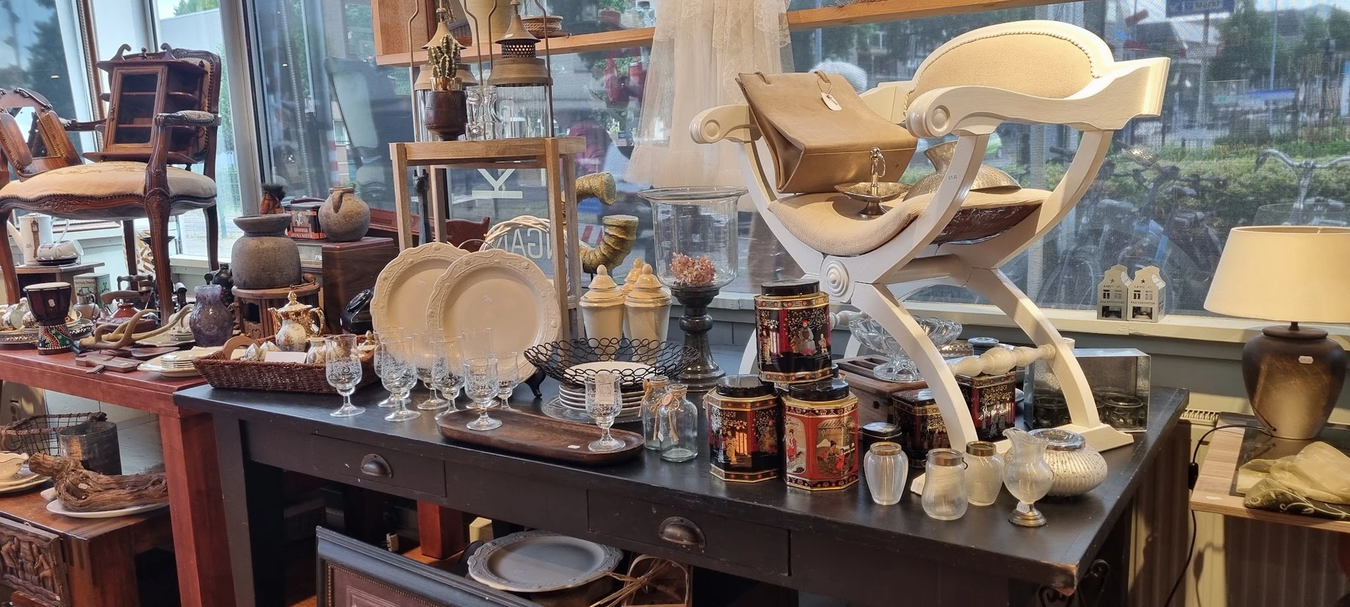 Uitgestalde vintage serviesgoed, glazen en decoratieve huishoudartikelen op een donkere toonbank
