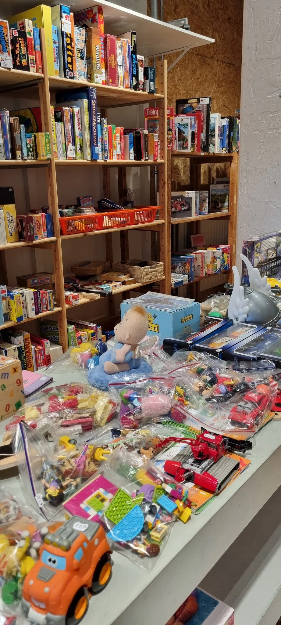 Speelgoed en boeken uitgestald op tafels voor de winkelschappen, waaronder knuffelbeesten, spellen en kinderboeken