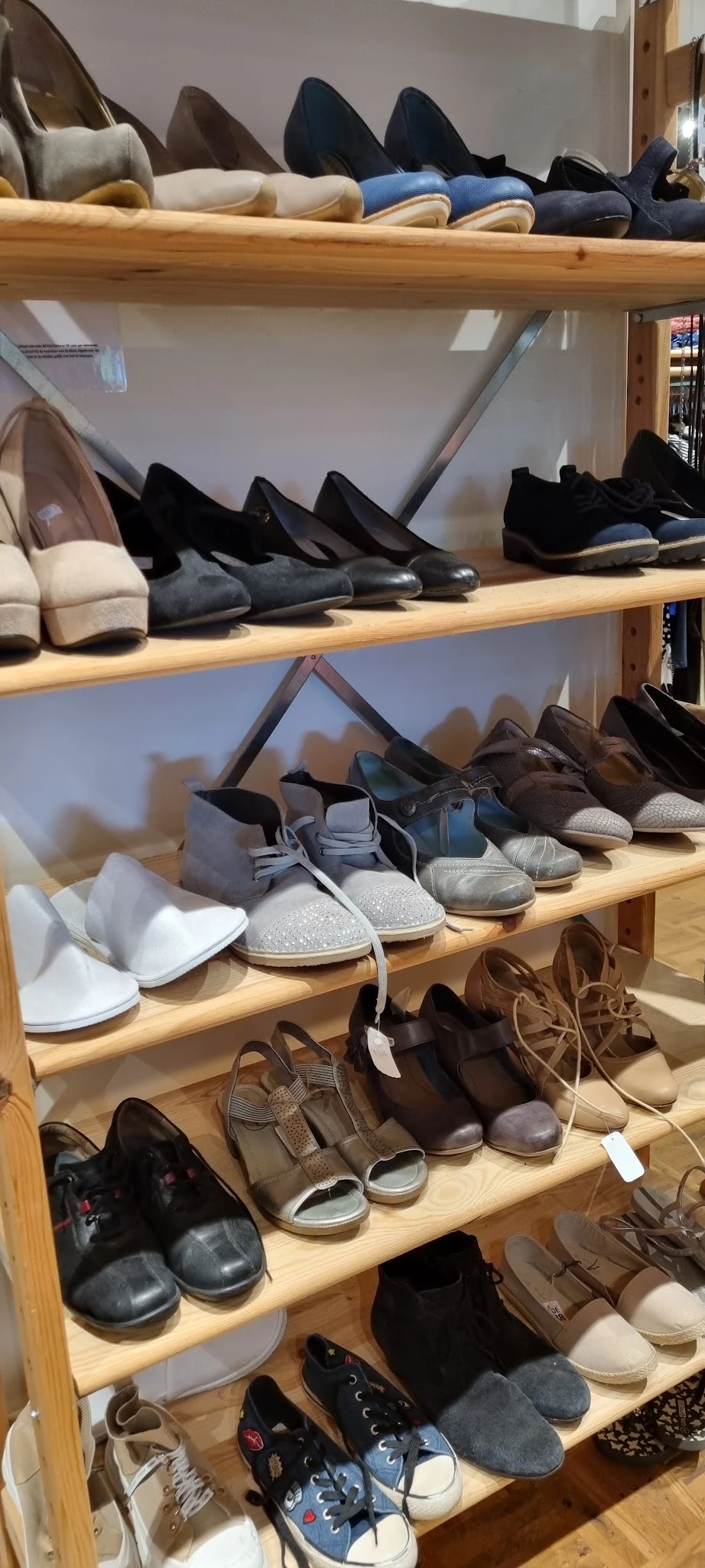 Houten schappen met diverse schoenen en slippers, waaronder witte, blauwe, bruine en zwarte modellen