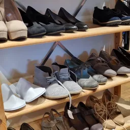 Houten schappen met diverse schoenen en slippers, waaronder witte, blauwe, bruine en zwarte modellen