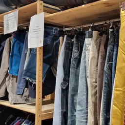 Houten stellingen met tweedehands broeken, jeans en andere kleding aan hangers