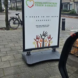 Wit bord met tekst '7 DAGEN IN DE WEEK GEOPEND' en gekleurde handen, openingstijden vermeld