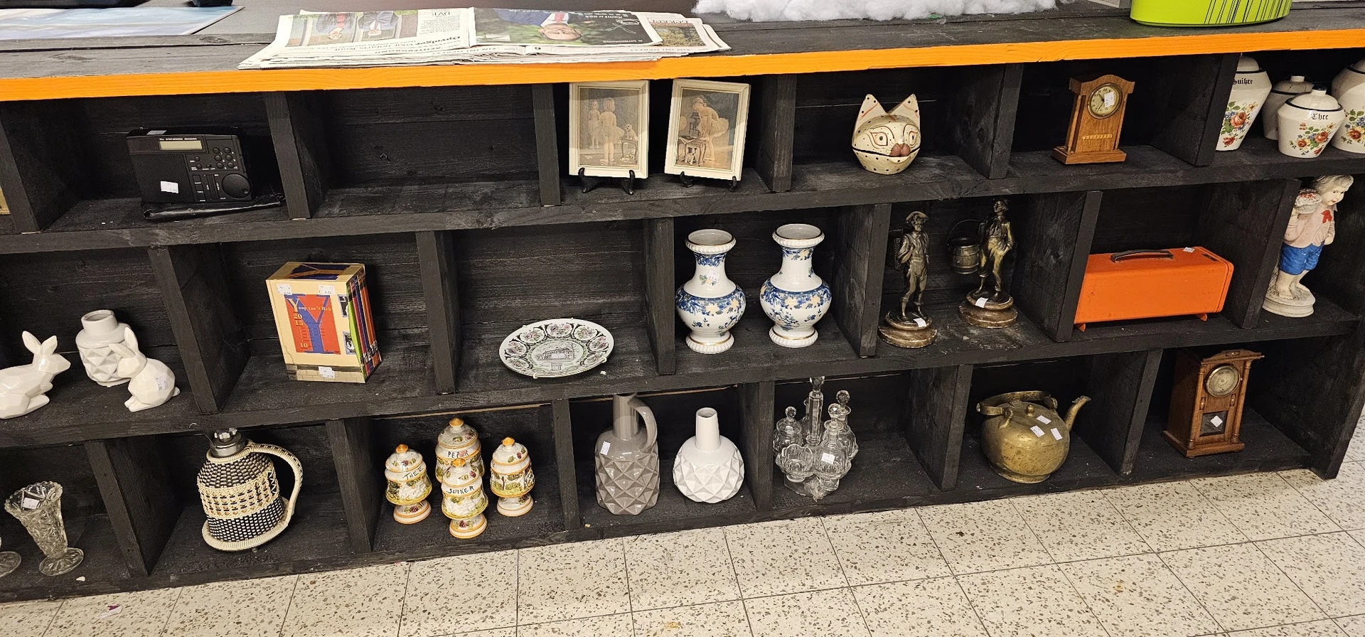 Zwarte wandkast met decoratieve items: porselein, beeldjes, boeken en huishoudartikelen