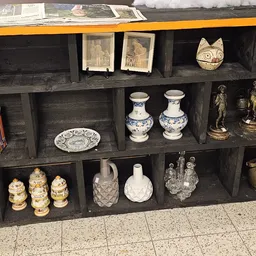Zwarte wandkast met decoratieve items: porselein, beeldjes, boeken en huishoudartikelen