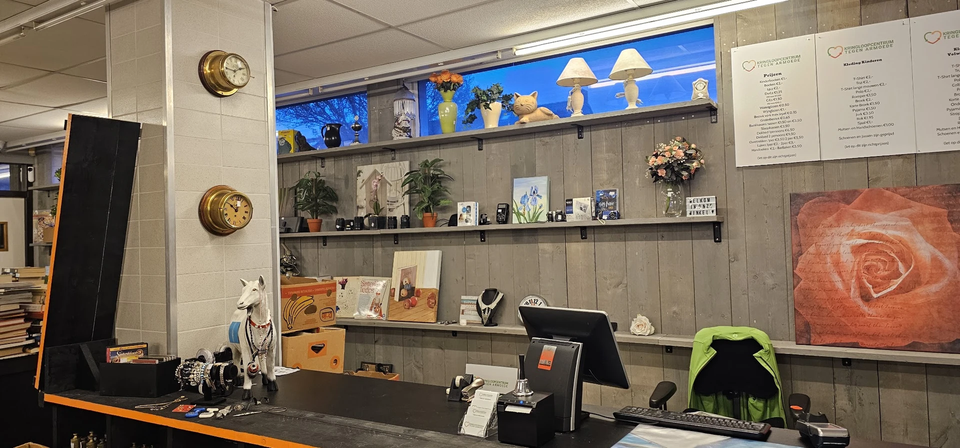 Werkplek met zwarte bureau, computer en achter grijze wandplanken met decoratie, plantjes en diverse objecten