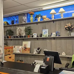 Werkplek met zwarte bureau, computer en achter grijze wandplanken met decoratie, plantjes en diverse objecten