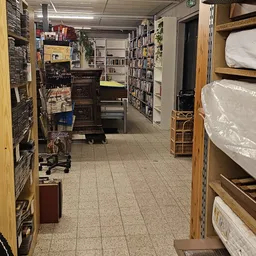Winkelinterieur met boekenrekken, een donkere houten kast, bedden met matrassen en diverse huisraad langs de wanden