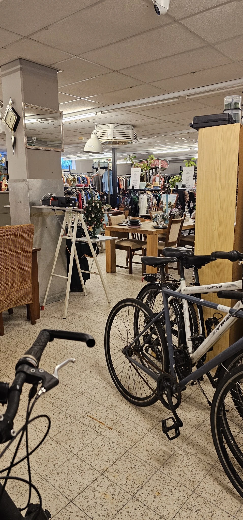 Winkelinterieur met fietsen, kledingrekken, houten tafels en stoelen tussen stellingen