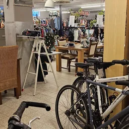 Winkelinterieur met fietsen, kledingrekken, houten tafels en stoelen tussen stellingen