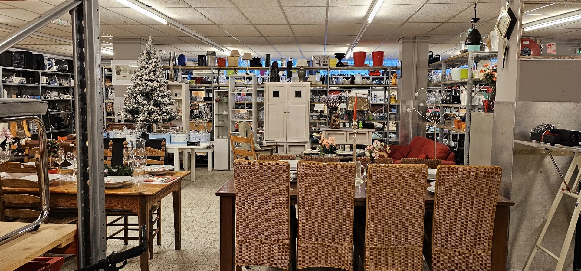 Winkelvloer met tafels, stoelen, kasten en stellingen vol met tweedehands spullen en een versierde kerstboom